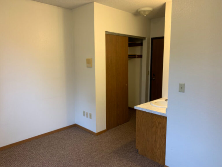 Empty room with bathroom entrance and carpeted floor.